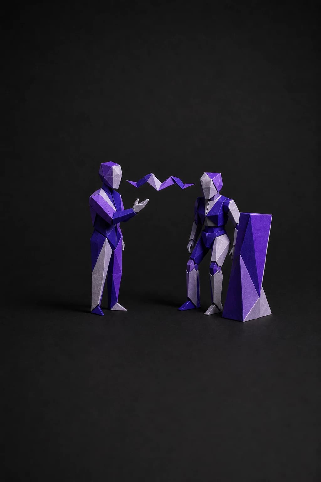 Escultura de papel plegado: una figura habla y otra escucha, junto a un panel en pie